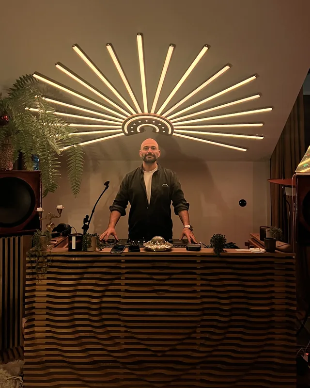 Kayvan behind his DJ booth under a sunburst light